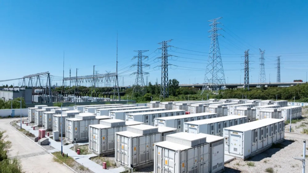 Reihen von Batteriespeicher-Containern vor Hochspannungsleitungen